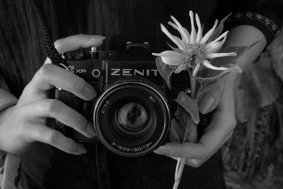 Close-up of a vintage Zenit camera held with a flower, in black and white.