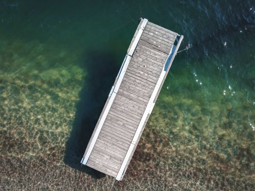 Free Drone shot of a wooden dock extending over clear green lake waters, viewed from above. Stock Photo