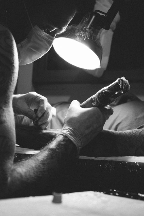 Free Black and white photo of a tattoo artist at work under bright light, highlighting his skills. Stock Photo