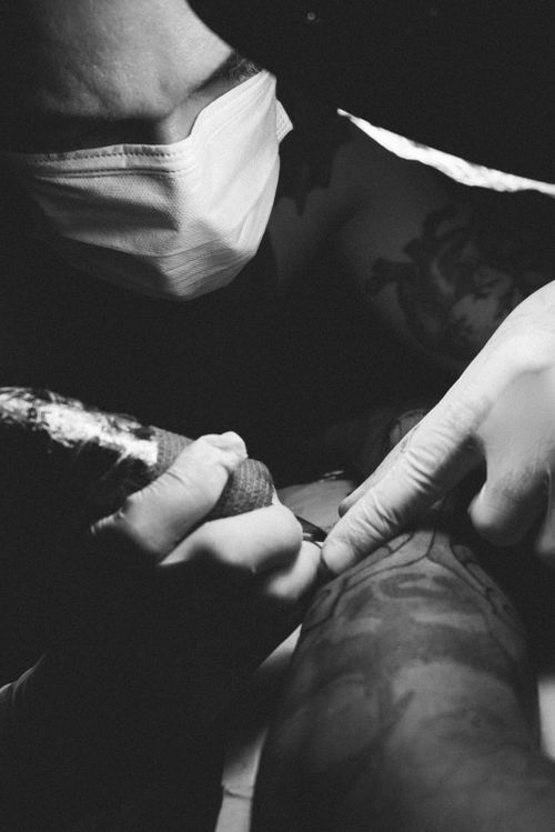 Free Black and white image of a tattoo artist carefully working on an intricate arm tattoo using a tattoo machine. Stock Photo