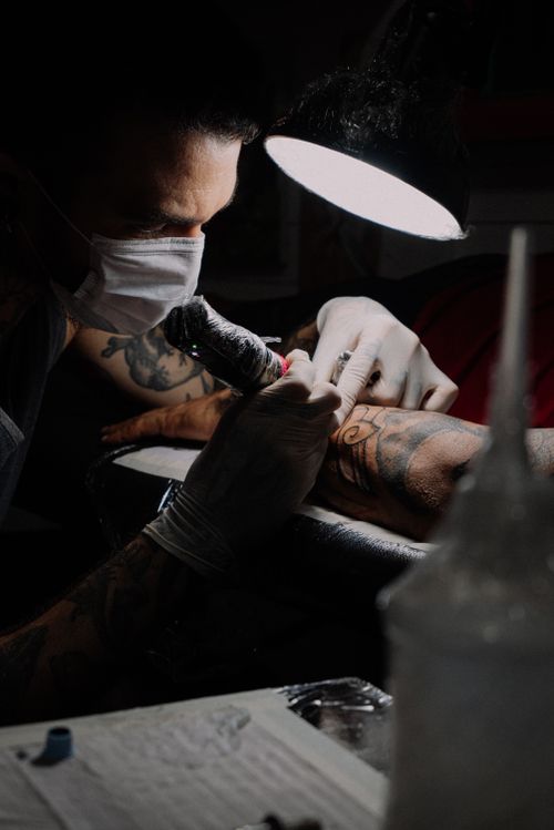 Free Tattoo artist focused on creating a detailed design under bright studio lighting. Stock Photo