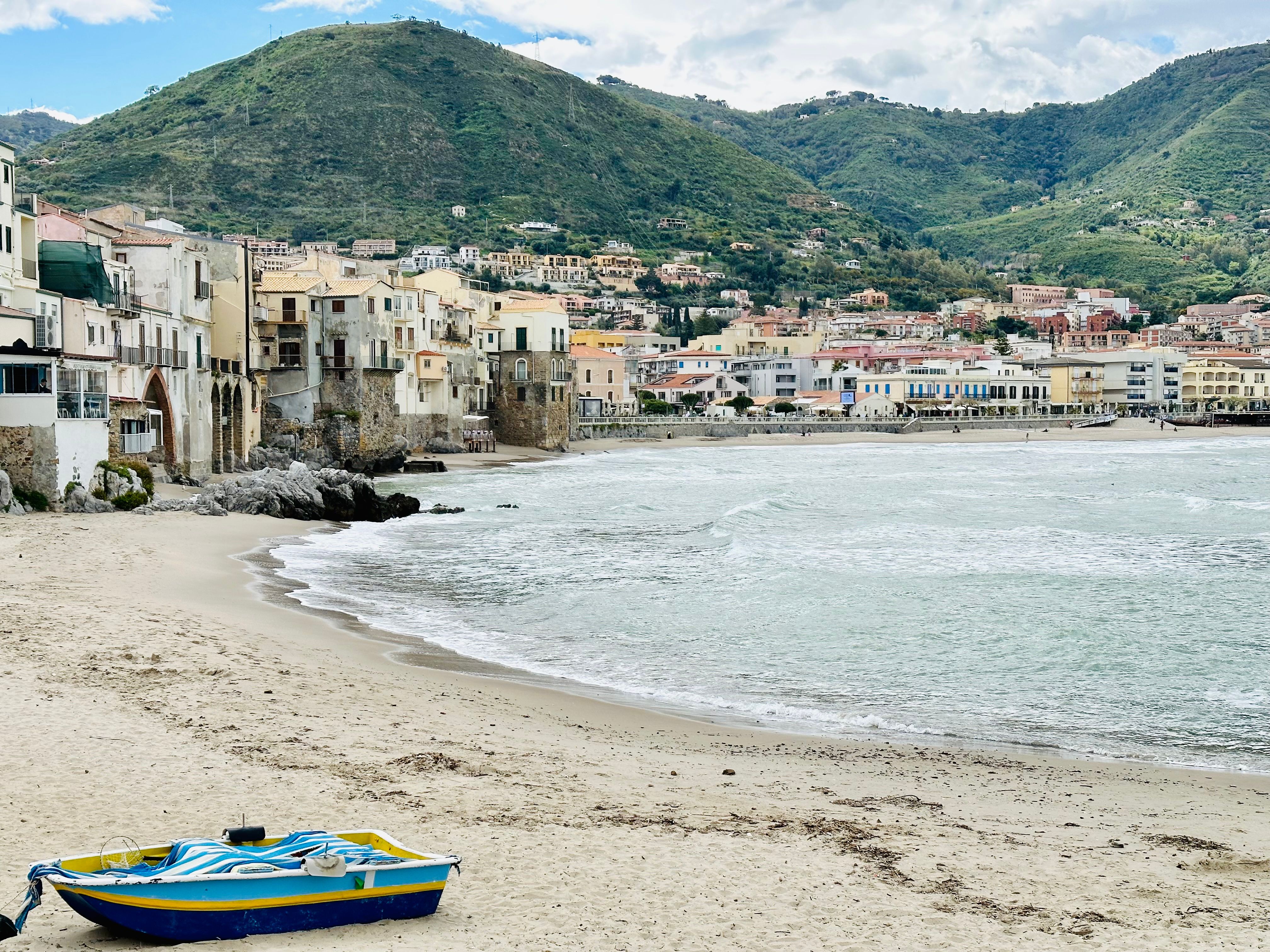 A picturesque coastal town with hills and a sandy beach featuring architecture and a boat on the shore.