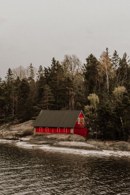 A cozy red cabin nestled by a tranquil forested shoreline in Stockholm, Sweden.