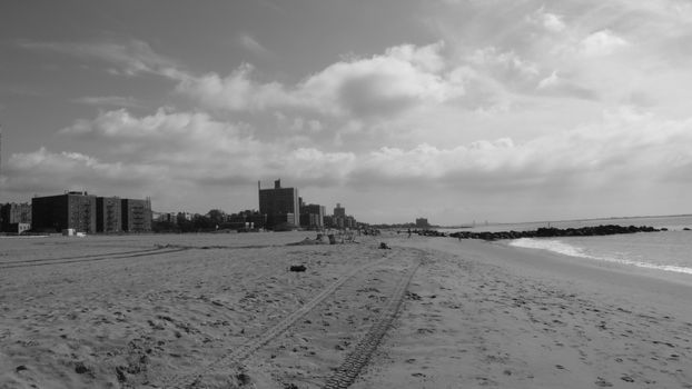 Monochrome view of a city beach with distant buildings and cloudy sky.