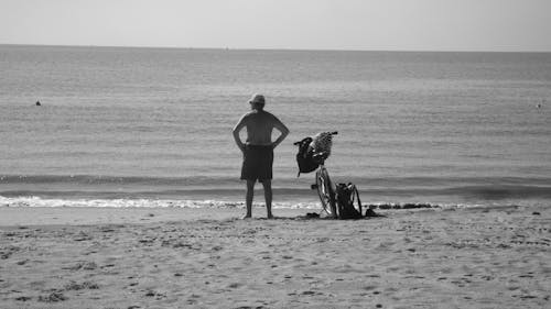 Black and White Photograph of a Man Standing with a Bicycle on a Seaside