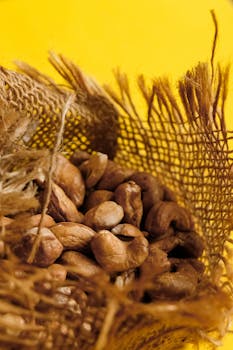 Close-up of roasted cashew nuts in burlap sack with a vibrant yellow backdrop.