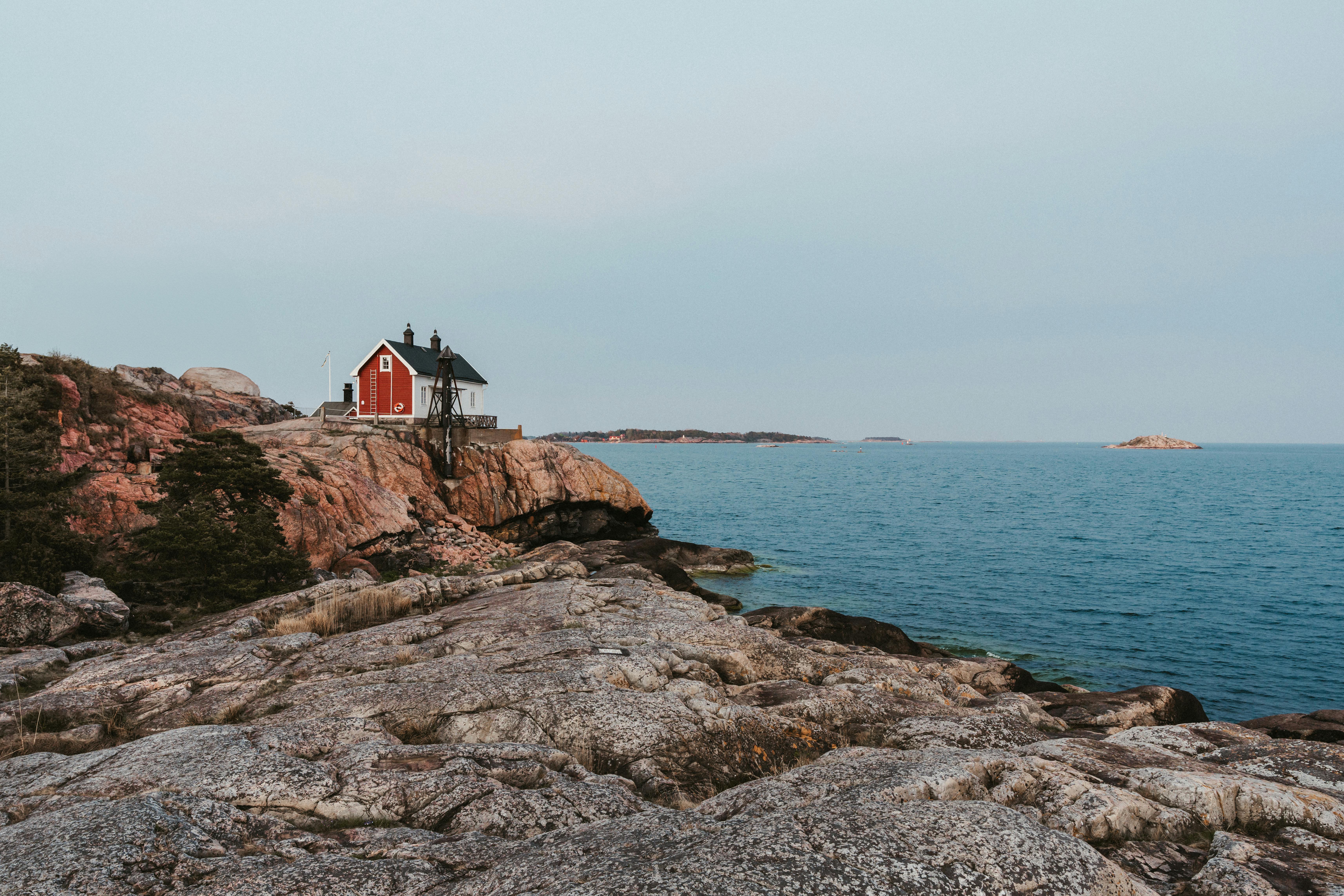 Picturesque view of a red cottage by the rocky coast and sea, surrounded by nature.