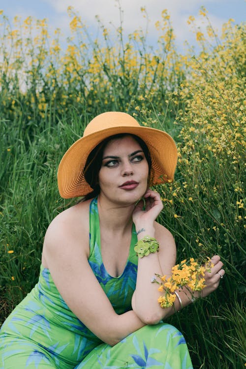 Woman Wearing a Green Dress Posing in Meadow with Yellow Flowers