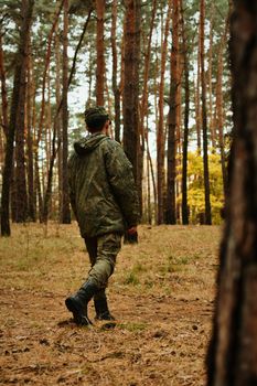 A soldier in camouflage uniform walking through a pine forest, showcasing military themes.