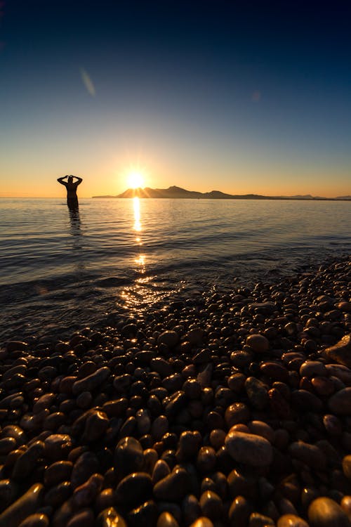 Person Standing on Sea Shore at Sunset
