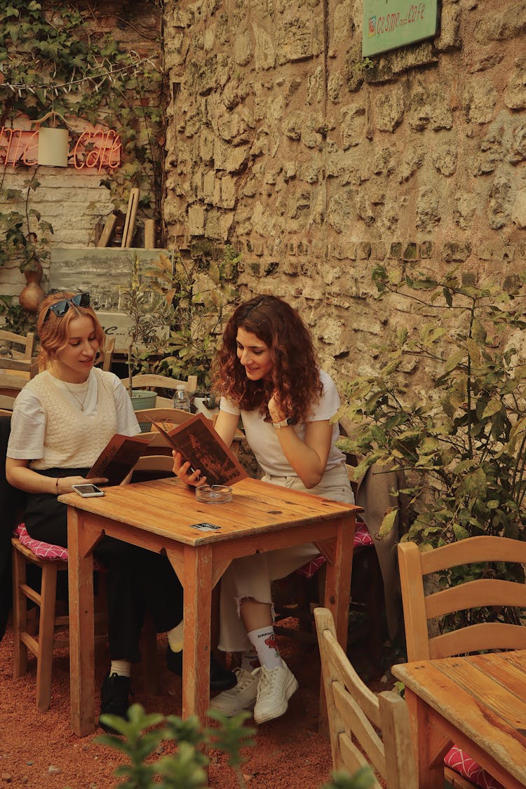 Women Sitting By Table And Browsing Menus