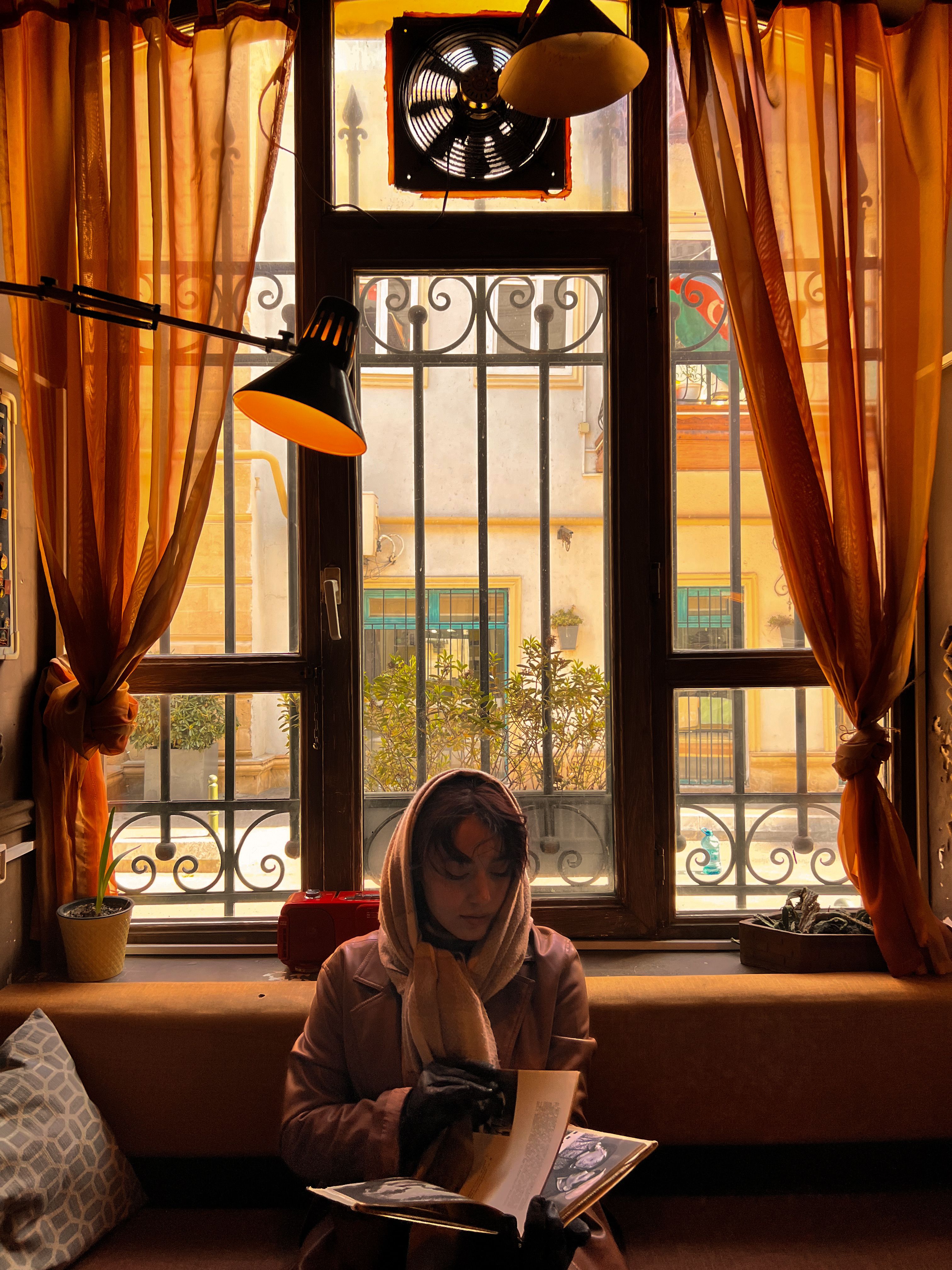 A woman in a hijab reads quietly by a sunlit window, creating a warm, serene atmosphere.. woman, hijab, reads