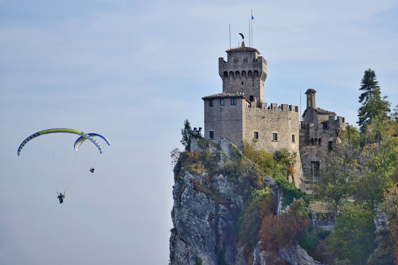 paragliders soar near the iconic san marino castle perched on a cliff