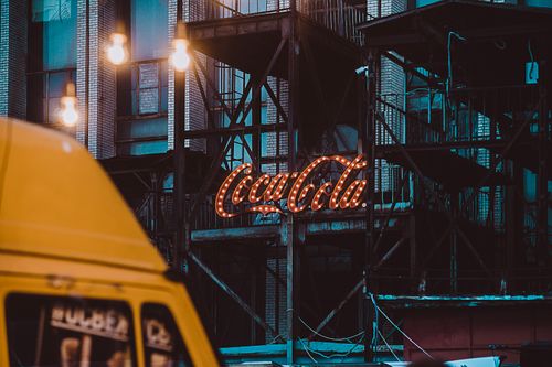Free Dramatic urban street scene featuring a neon Coca Cola sign on an industrial building. Stock Photo