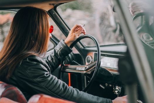 A stylish woman smoking inside a vintage car, showcasing a relaxed and nostalgic atmosphere.