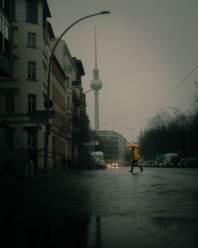 A rainy, foggy street in Berlin featuring the Berliner Fernsehturm and a pedestrian with an umbrella.