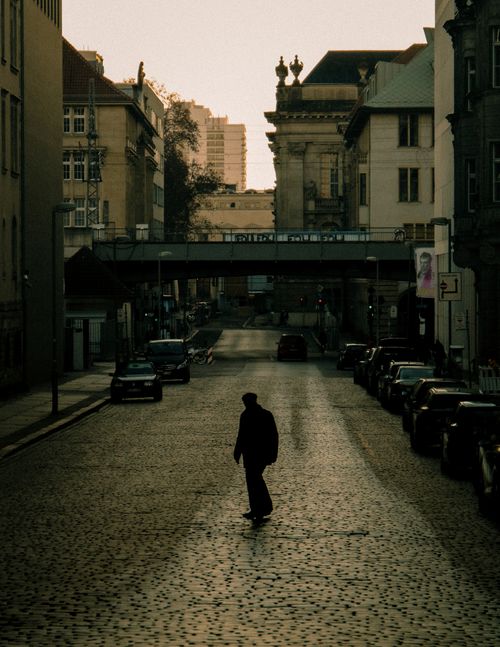Free Silhouette of a man walking on a cobblestone street in a city during sunset, showcasing urban architecture. Stock Photo