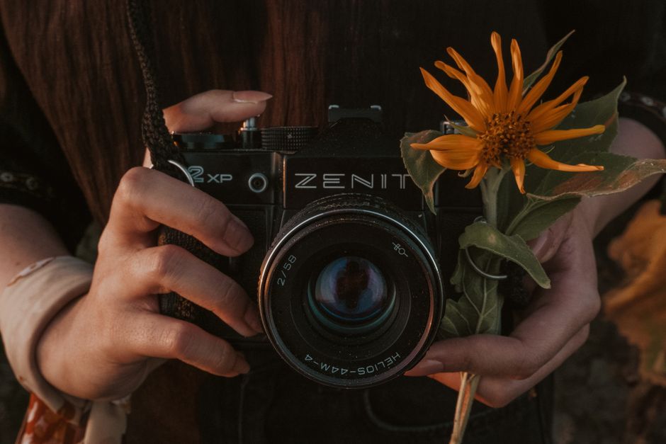Close-up of hands holding a Zenit film camera adorned with a vibrant yellow flower.