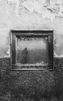 A black and white photo of an abandoned building with a cracked window reflecting a silhouette.