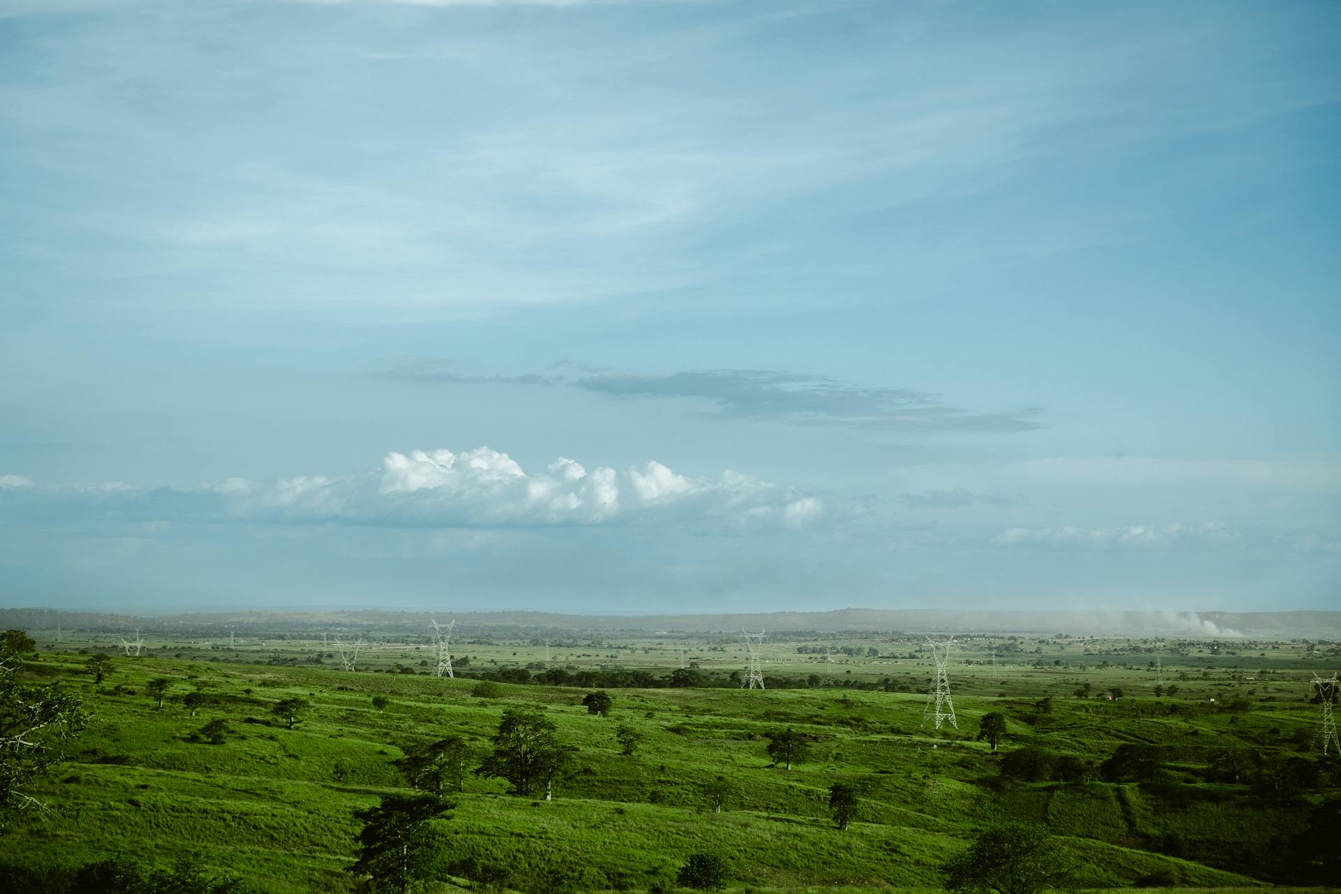Explore the sprawling green plains of Luanda with expansive skies and distant power lines.