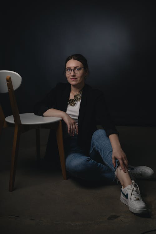 Woman in Eyeglasses Sitting on the Floor by the Chair 