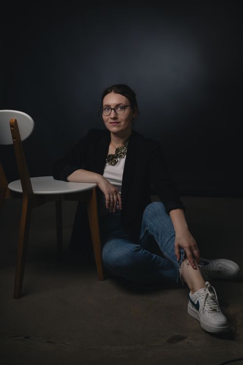 Free Young woman in casual fashion sitting on the floor indoors with a chair, wearing eyeglasses and smiling. Stock Photo
