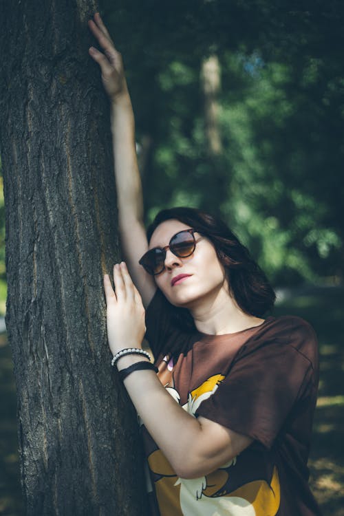 Woman in Sunglasses and T-shirt Standing by Tree