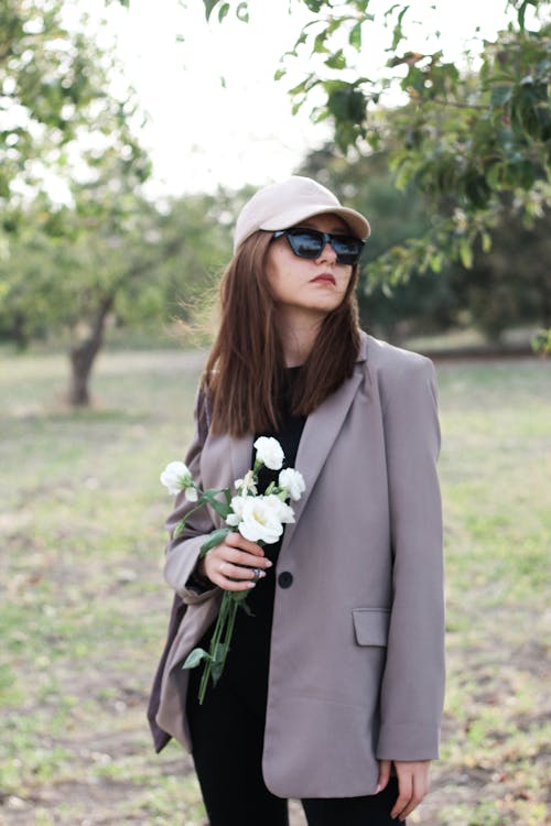 Woman in Jacket, Sunglasses, Cap and with Flowers