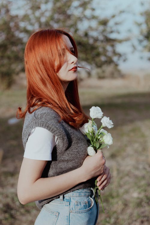 Young Redhead Standing on a Meadow and Holding Flowers