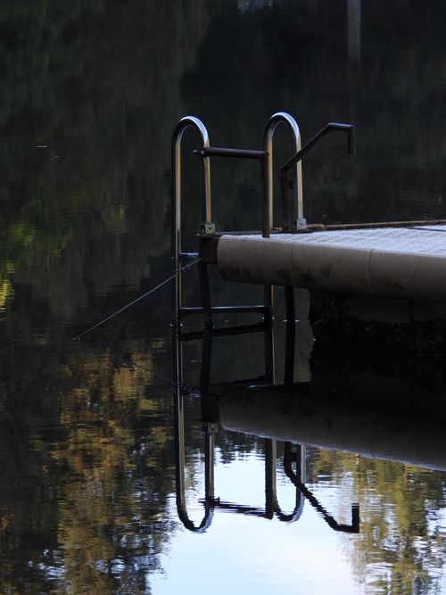 Free A tranquil lakeside pier with ladder reflecting serenely on calm water in Saint-Laurent-les-Églises, France. Stock Photo