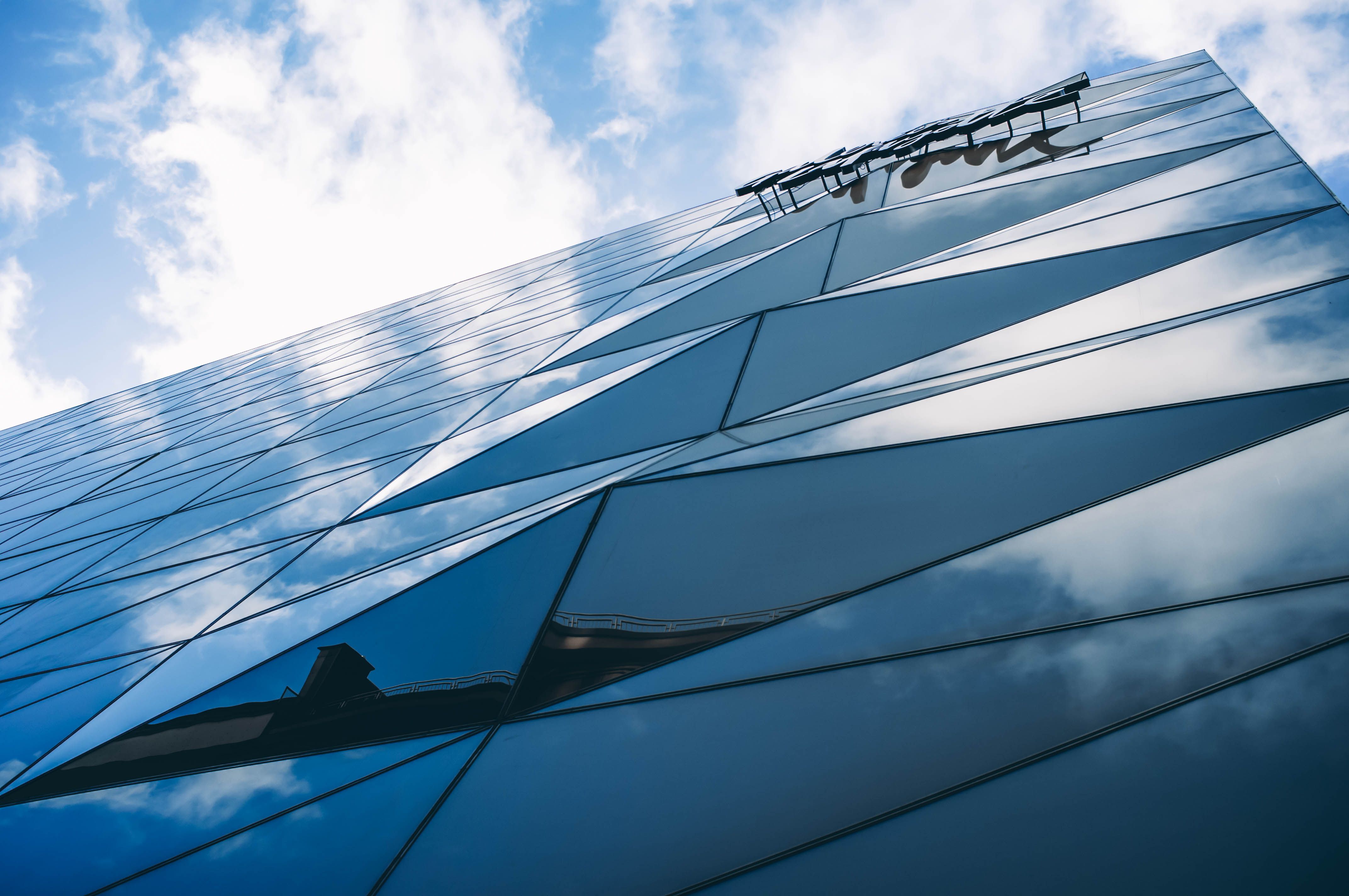 Low angle photo of a modern glass office building in Luxembourg city reflecting the sky.