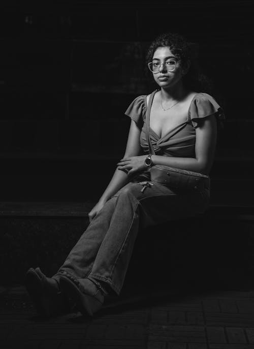 Young Woman in a Casual Outfit Sitting on the Steps in the Dark 