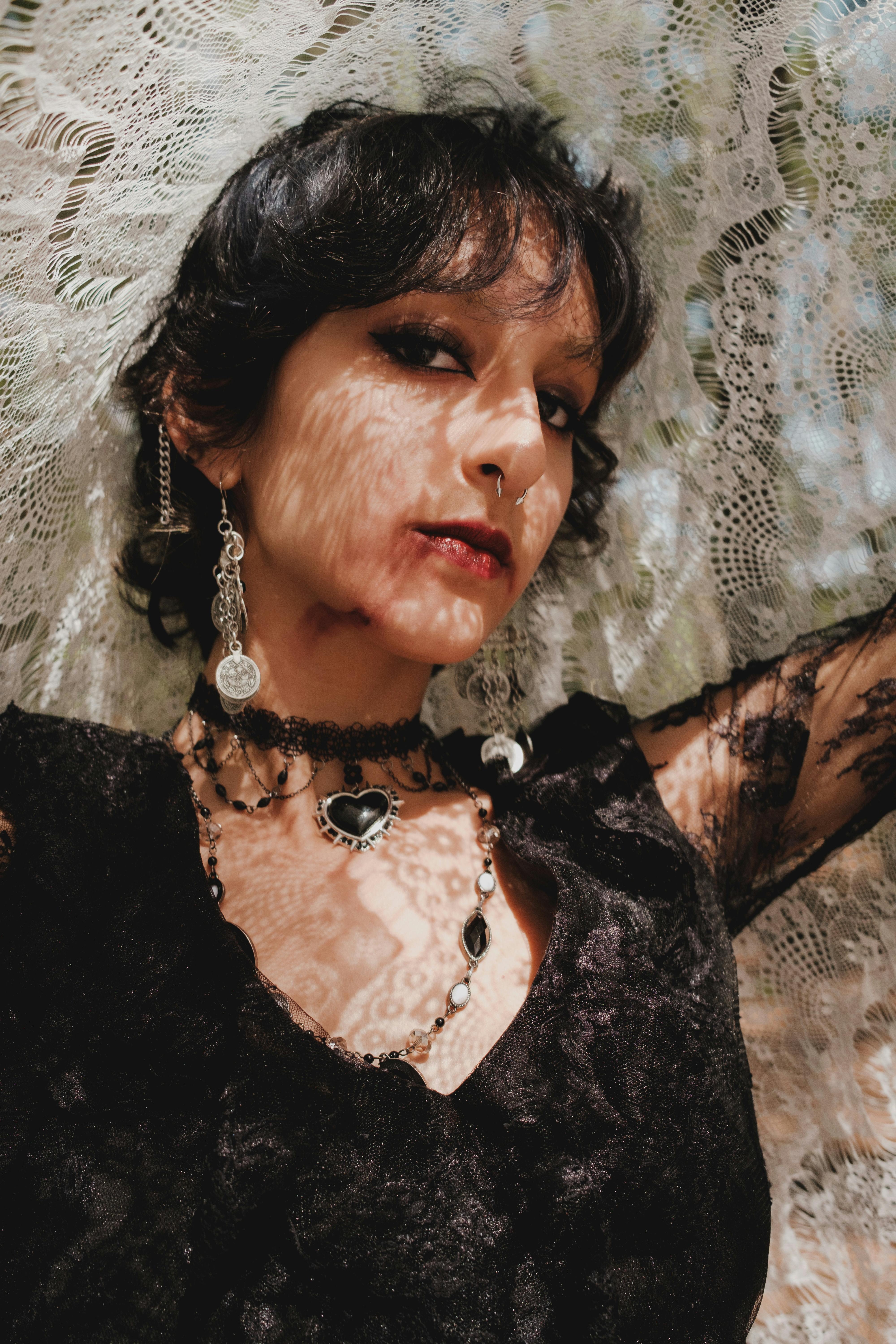 Close-up portrait of a woman in gothic attire with lace shadows on her face.
