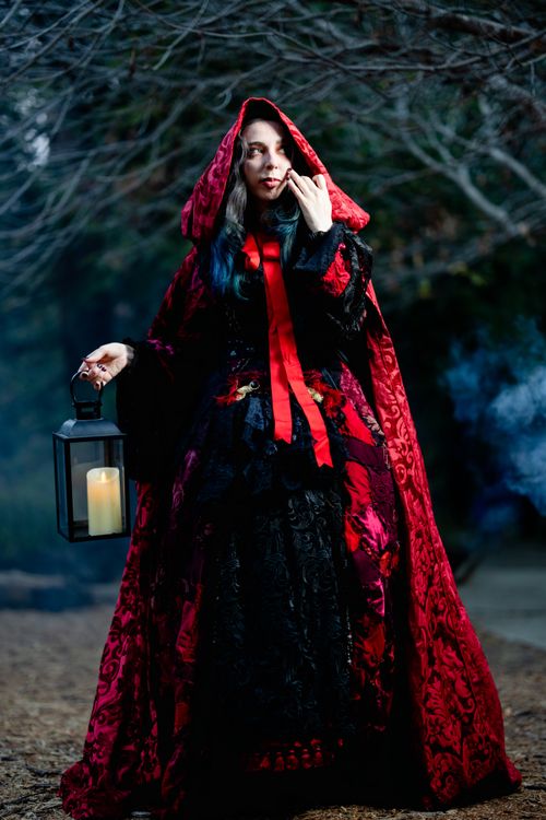 Free Gothic woman in a red cape holding a lantern in a mysterious forest setting. Stock Photo