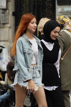 Two women walk on a busy street, showcasing diverse fashion styles.