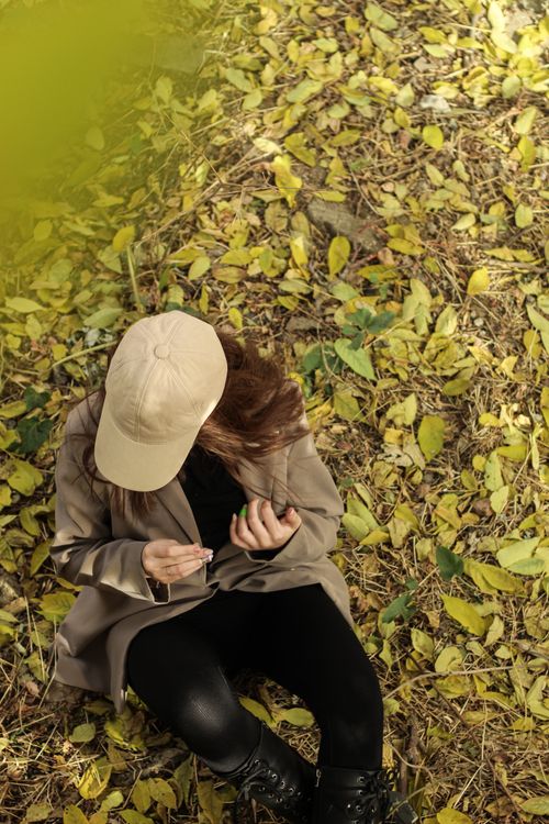 Free A woman wearing a beige cap sits amidst fallen yellow autumn leaves. Stock Photo