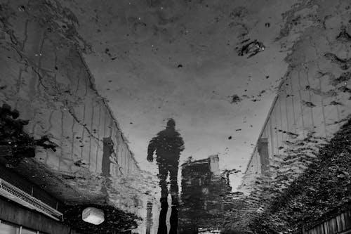 Reflection of a Person Walking on the Street and Buildings in a Puddle 