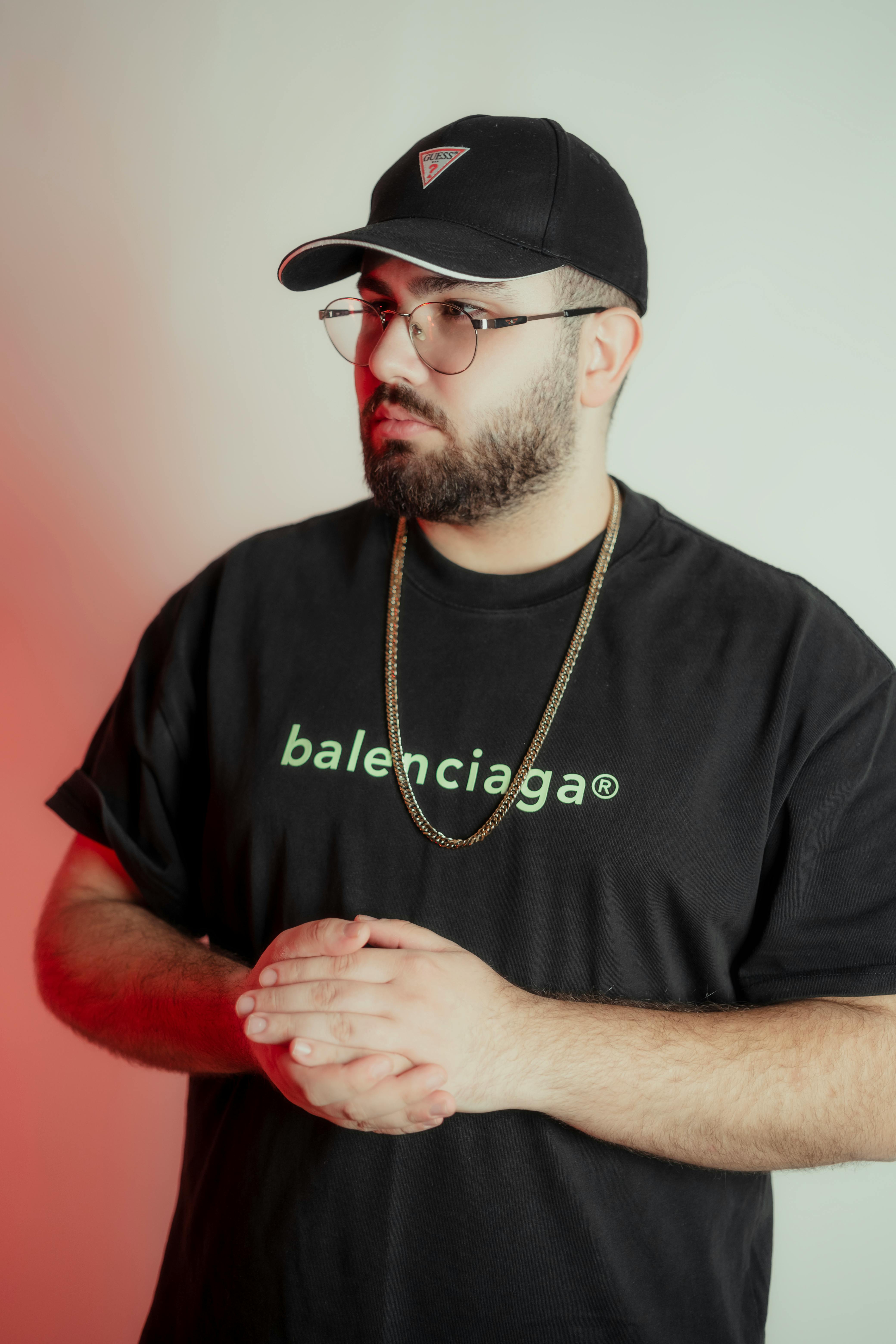 Close-up portrait of a man in a black t-shirt, cap, and glasses with a contemplative pose.