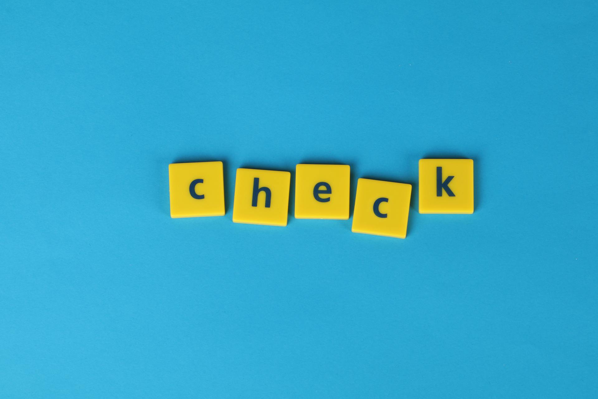 Yellow letter tiles spelling 'check' on a vibrant blue background, conveying approval or verification.