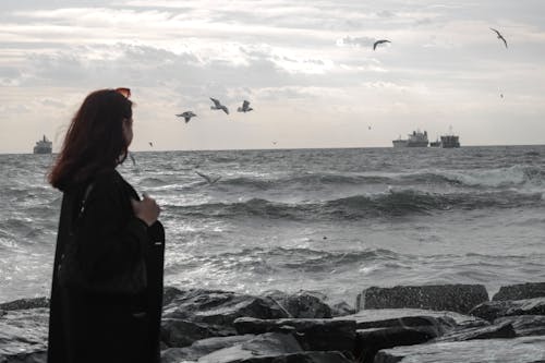 Woman Standing on Sea Shore with Seagulls Flying around