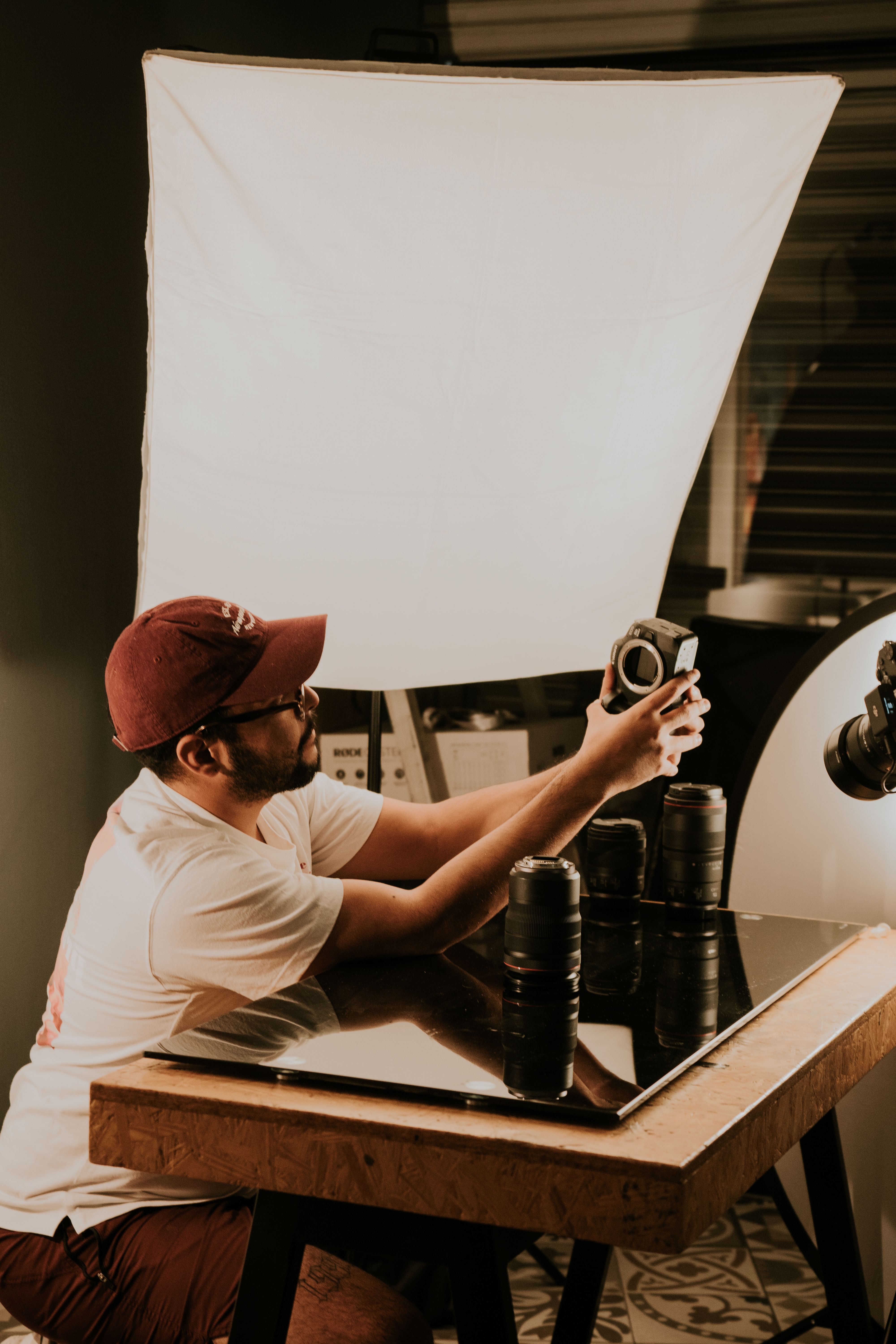 Photographer inspects camera gear on a studio desk with professional lighting setup.