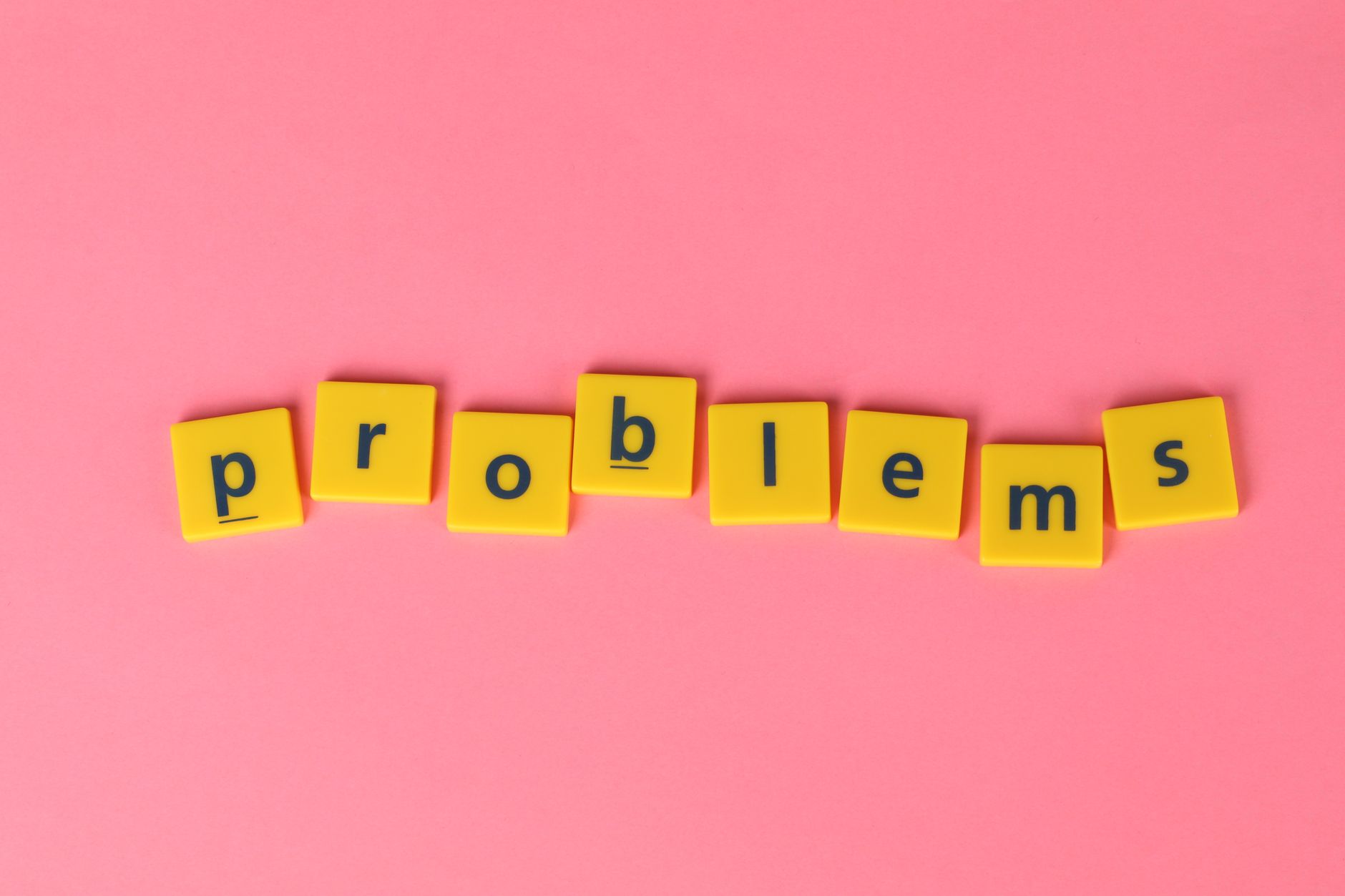 Yellow letter tiles spelling 'problems' on a contrasting pink background. Perfect for creative design projects.