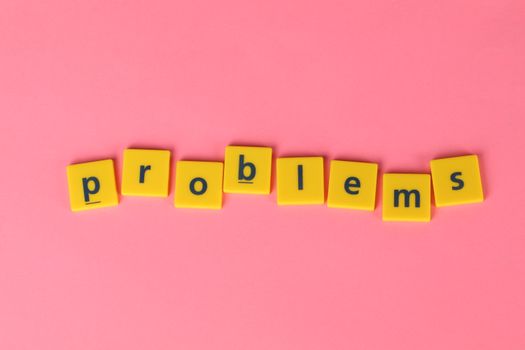 Yellow letter tiles spelling 'problems' on a contrasting pink background. Perfect for creative design projects.