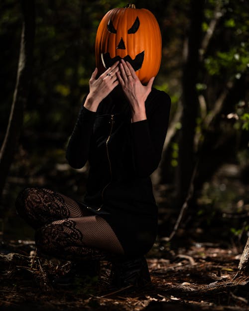 Woman in Black Dress with Pumpkin on Head Posing in Forest