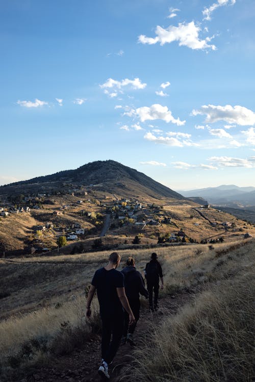 People Hiking on Footpath towards Village and Hill