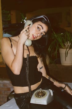 Stylish young woman sitting indoors using a vintage rotary telephone.