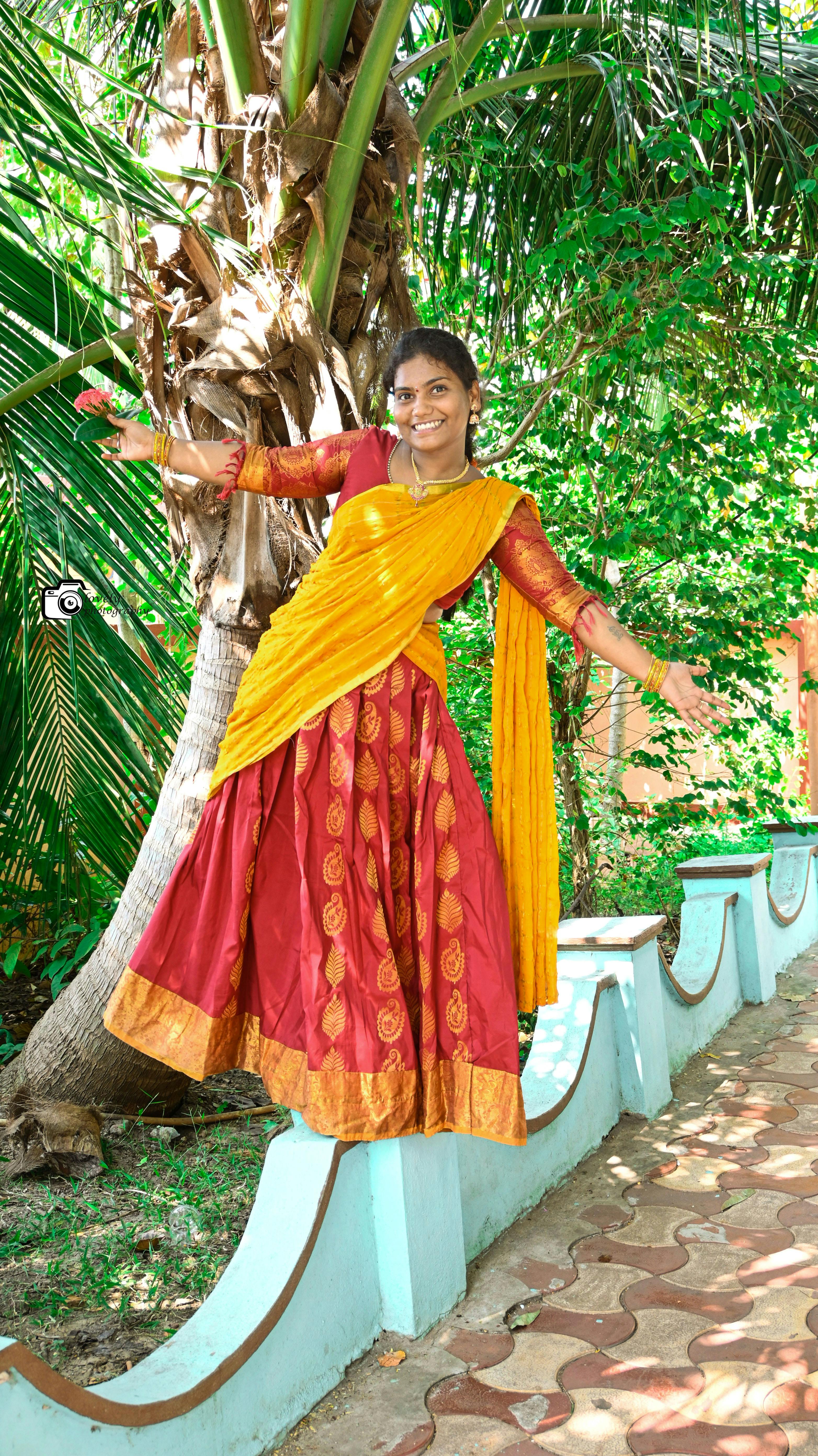 Smiling woman in vibrant sari poses playfully among lush greenery, showcasing Indian culture.