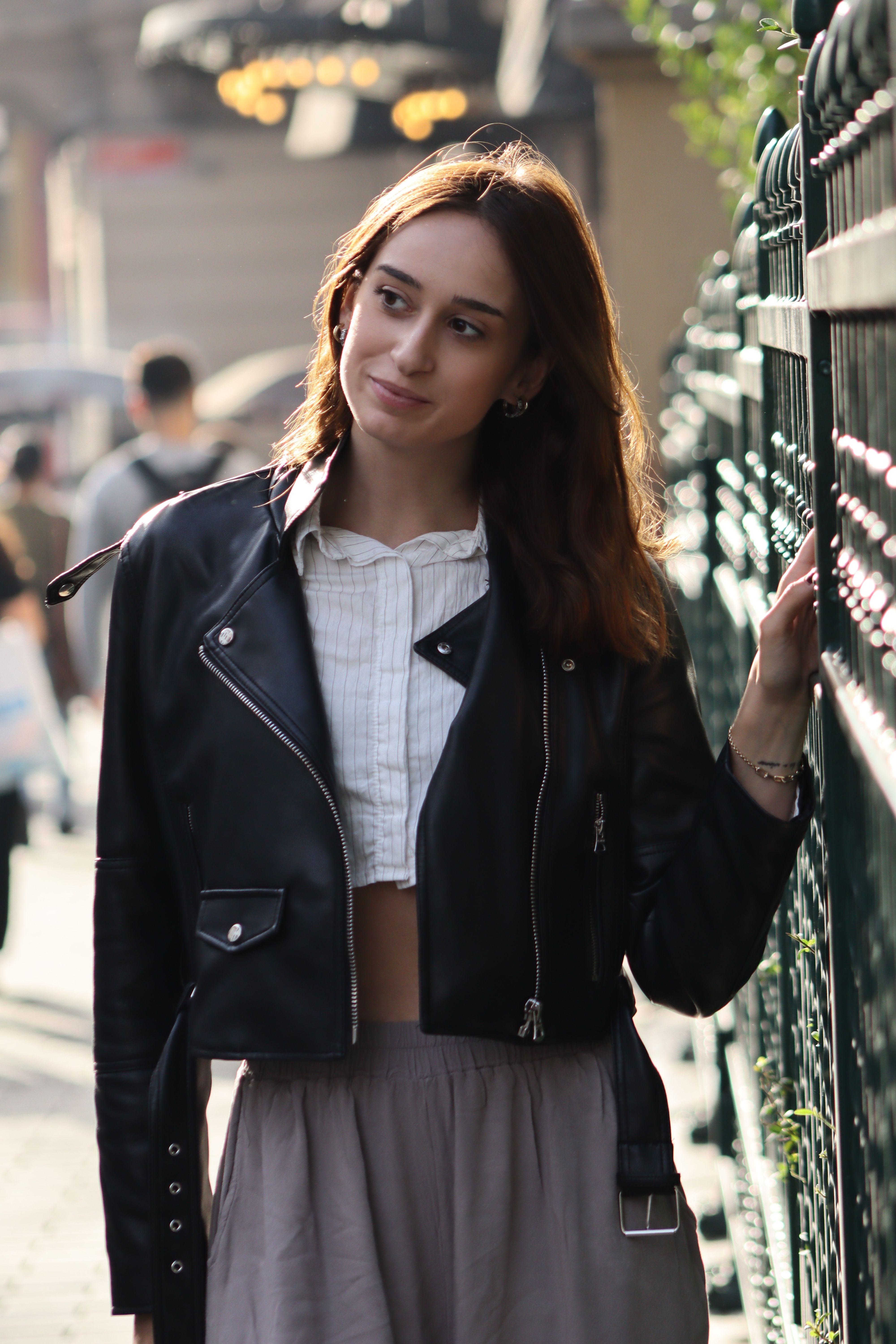 Fashionable young woman in leather jacket enjoying a sunny day outdoors.