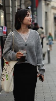 Stylish woman with a bag and coffee walking in a city street, embracing urban fashion.