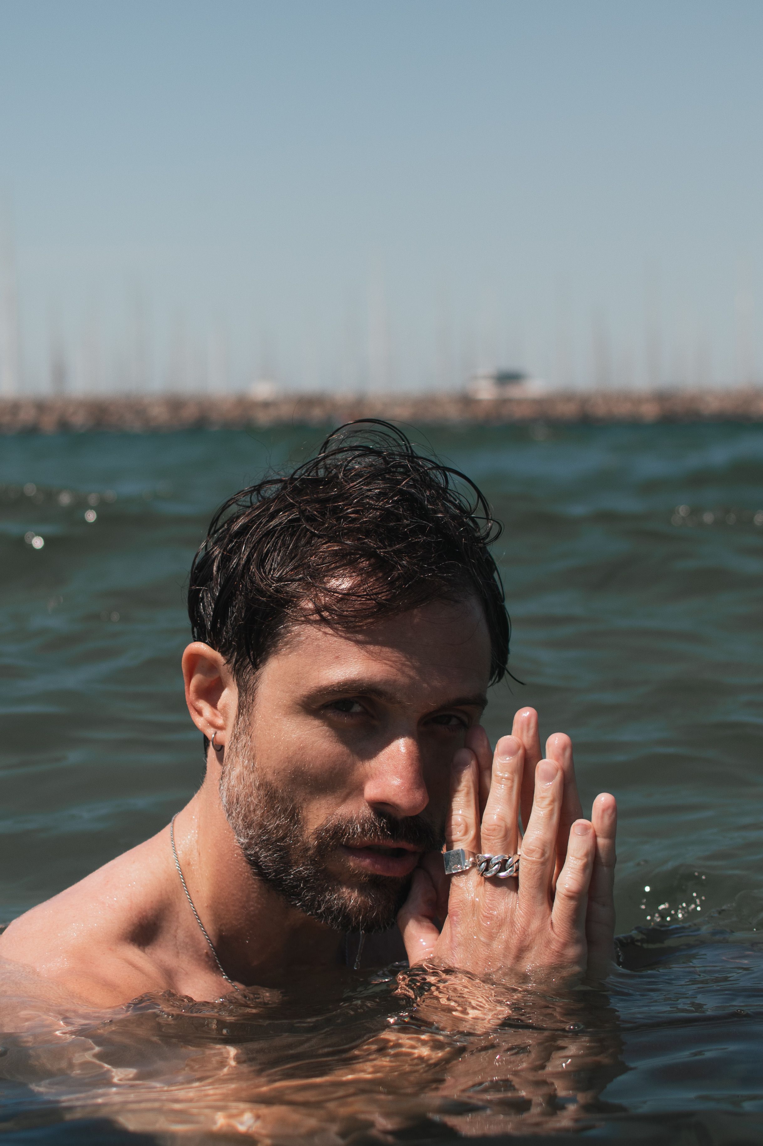 Portrait of a man with rings and beard submerged in the sea on a sunny day.